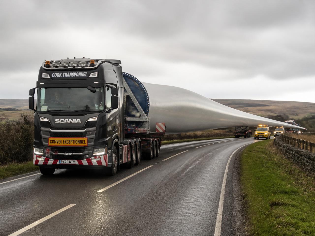 A UK Scania heavy haulage tractor pulling a wind turbine blade along a rural British road